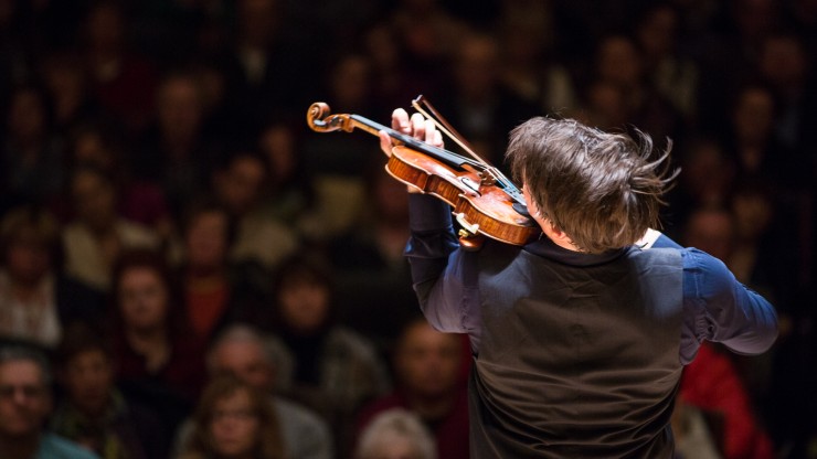 Violinist Joshua Bell plays his violin passionately while facing a large audience.