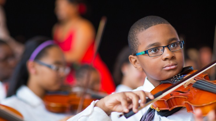 Kid playing violin in an orchestra