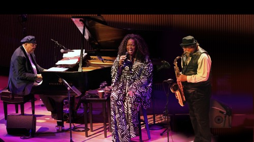 a male pianist, a female vocalist, and a male saxophonist perform together. 